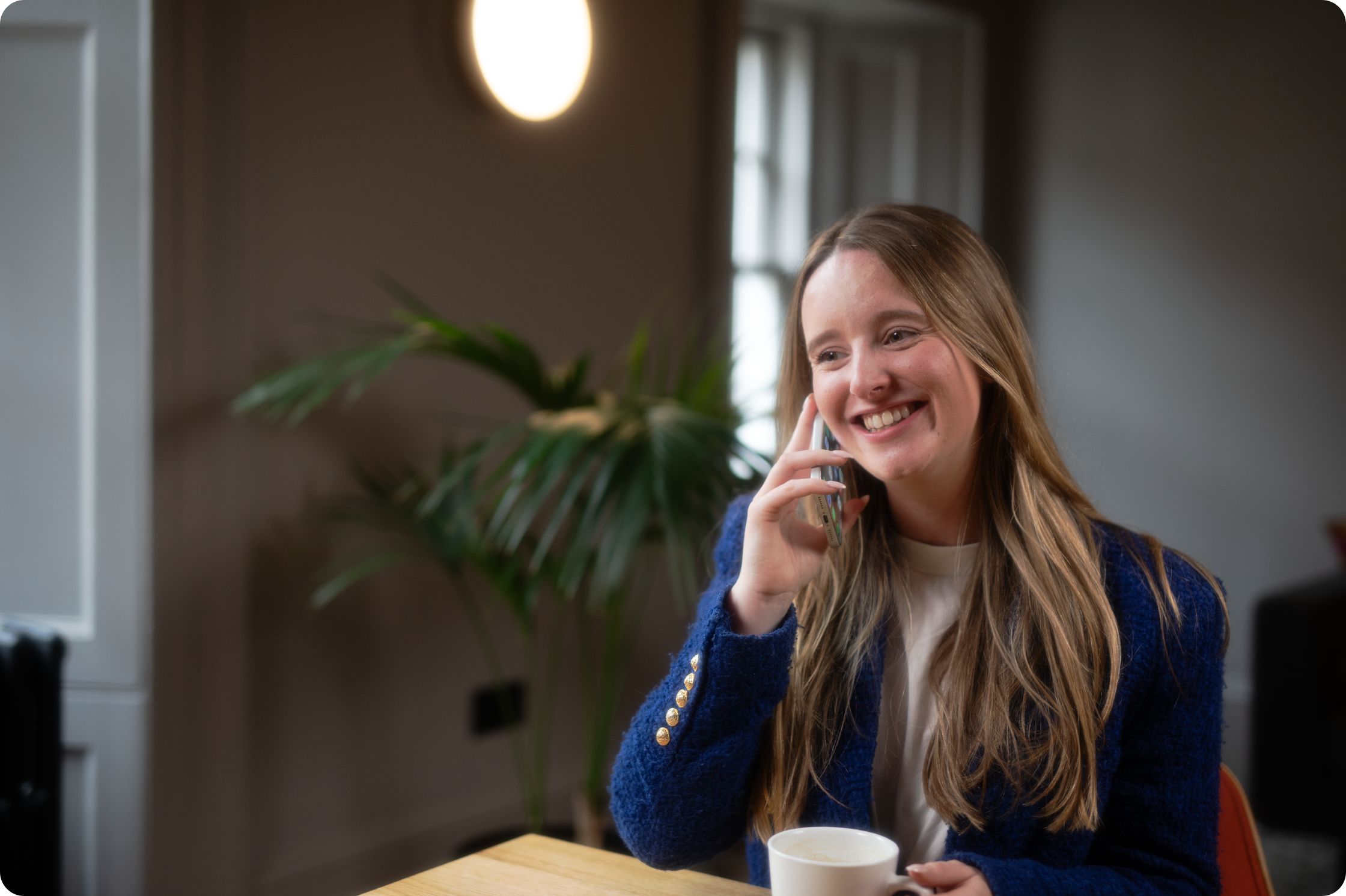 a woman on the phone, holding mug, sitting at desk