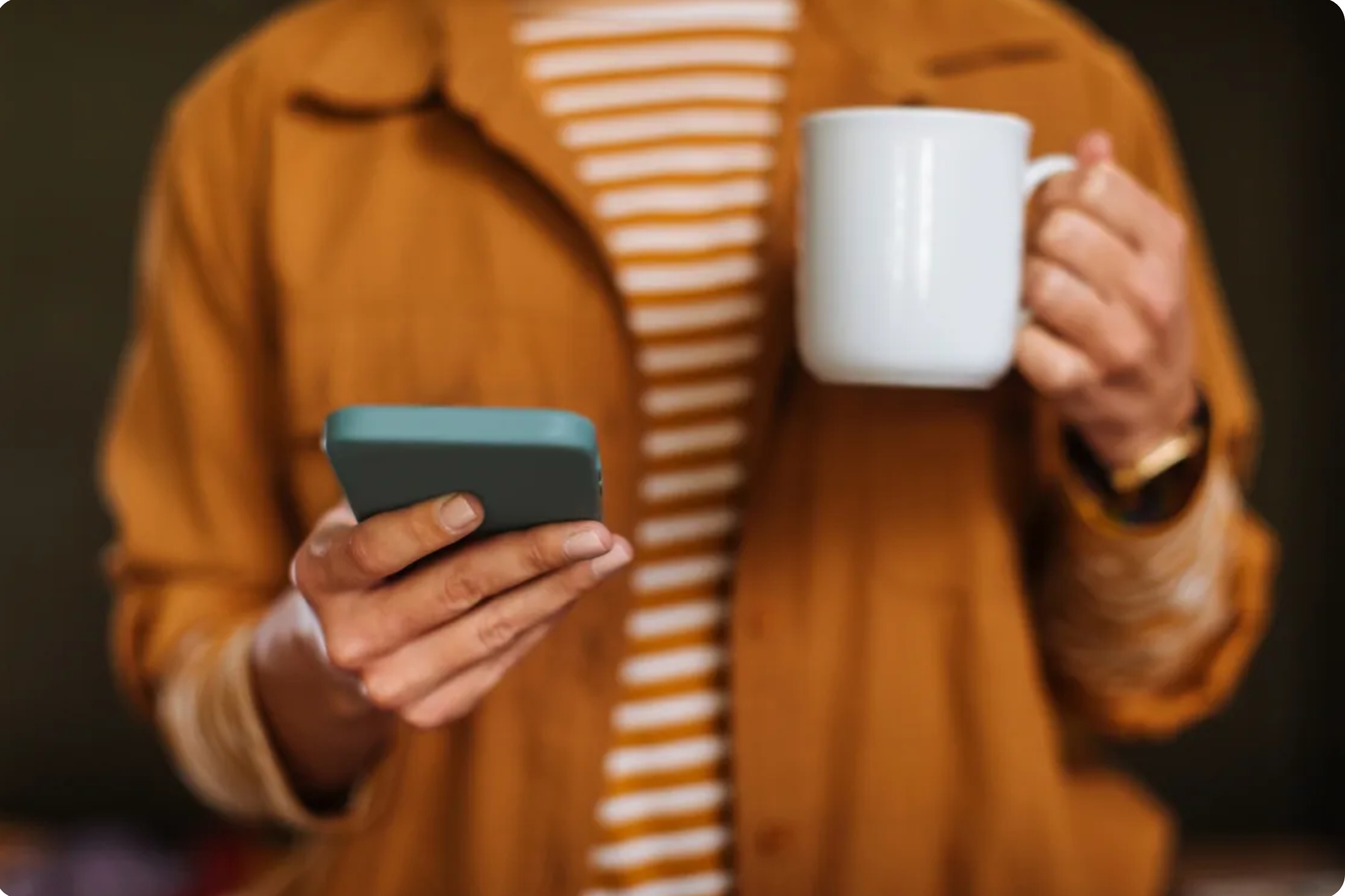 a person, holding a phone in one hand, mug in other, face not shown